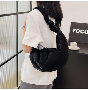Detail of a black crescent shoulder bag with unique pleated strap on a minimalist model