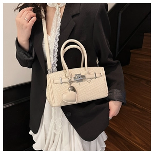 Detail of cream woven leather handbag featuring metal lock and heart charm accessory