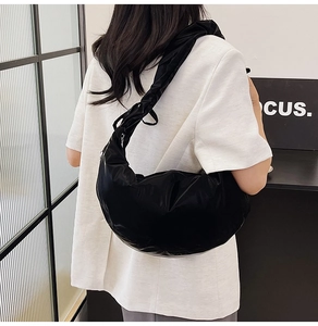 Detail of black glossy crescent bag with pleated shoulder strap on white blazer outfit
