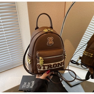 Détail d'un sac à dos en cuir marron avec écusson d'ours et clous dorés carrés