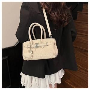Close-up of cream woven Kelly bag with heart charm and silver turn-lock on a model