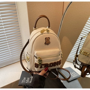 Détail de l'écusson d'ours en peluche et rivets dorés sur un sac à dos en similicuir
