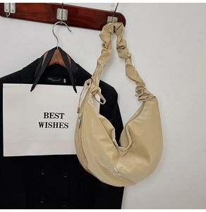 Detail of glossy beige crescent bag with pleated shoulder strap hanging on a wooden hook