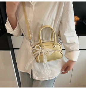 Detail of yellow pebbled leather crossbody bag with lace bow and pearl charm