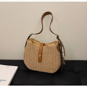 Detailed view of beige woven straw bucket bag with brown leather straps and gold buckle