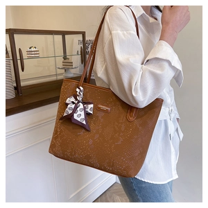Detail of a brown snakeskin tote bag with a heart-patterned silk scarf on the handle