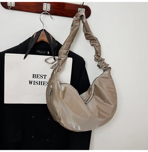 Detailed view of khaki hobo bag with pleated shoulder strap hanging on a black blazer