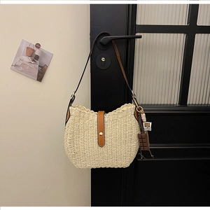 Detail of hand-woven straw hobo bag with brown leather strap and chocolate charm