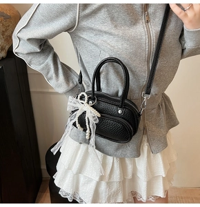 Close-up of black litchi pattern leather bag with white lace bow and pearl charms
