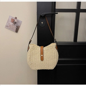 Detail of woven straw bucket bag with brown leather strap and golden metal buckle