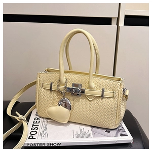 Detail of light yellow woven texture handbag with metal buckle and heart charm