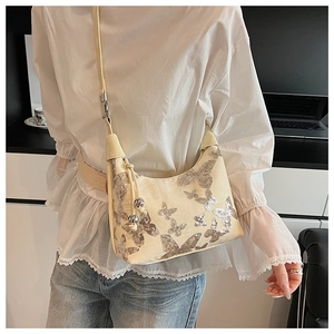 Close-up of a cream shoulder bag with sparkling silver sequin butterfly patterns and metal beads