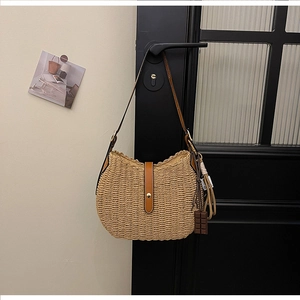 Close-up of woven crescent straw bag with leather strap and tassel hanging on a door handle