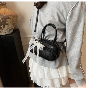 Detail of black mini crossbody bag with lace bow and pearl pendant on model