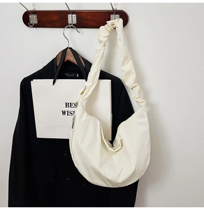 Detail of a creamy crescent bag featuring a pleated wide strap and smooth leather texture