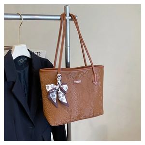 Detail of brown faux snake leather tote bag with silk scarf and logo on shoulder strap