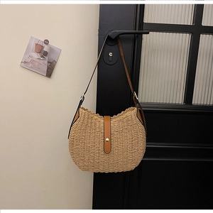 Detail of woven straw shoulder bag featuring brown leather trim and golden metal buckle