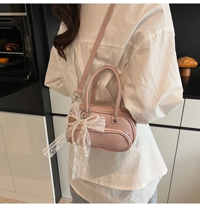 Close-up of pink pebbled leather handbag with lace bow and pearl charm on a model