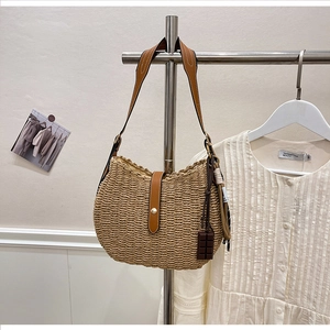 Detail of woven straw shoulder bag featuring leather strap and chocolate charm