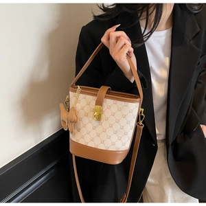 Détail d'un sac seau chic montrant un tissu à motifs beige avec bordure en cuir marron et fermoir doré