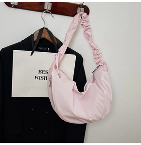 Detail of light pink crescent bag featuring stylish pleated shoulder strap and metal zipper