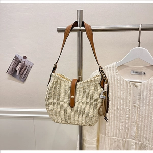 Detail of woven straw shoulder bag with dark brown leather straps and metal buckle