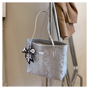 Close-up of silver tote bag with snake pattern embossing and polka dot bow detail