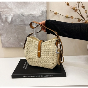 Detail of hand-woven straw bucket bag with brown leather strap and gold buckle accent