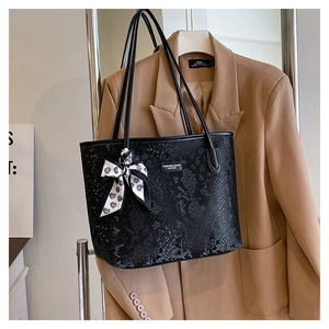 Detail of black snakeskin tote bag with heart scarf and fashion leather logo plate