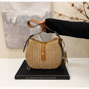Detail of woven straw shoulder bag with brown leather strap and tassel accent