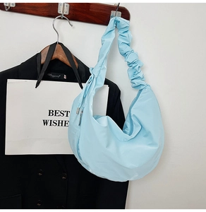 Detail of light blue crescent bag featuring pleated shoulder strap and silky nylon texture