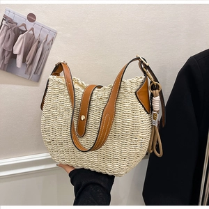 Detail of woven straw bucket bag with brown leather strap and contrast stitching