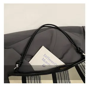 Detail of striped tote bag with black leather knotted handles and woven texture finish