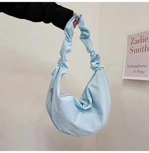 Detail of light blue crescent bag featuring pleated strap and smooth nylon texture