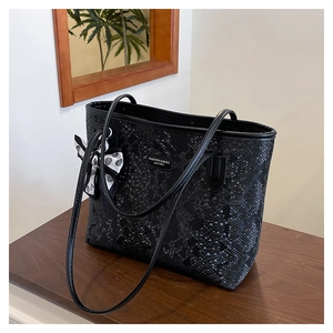 Detail of black faux snakeskin tote bag featuring a polka dot bow and metal logo tag