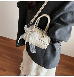 Close-up of beige leather mini crossbody bag with lace bow and pearl charms worn by a model