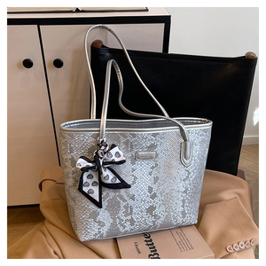 Detailed view of silver tote bag with snake texture and decorative heart bow on a blazer