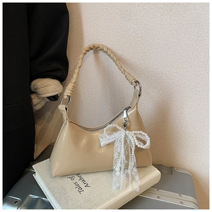 Détail du sac hobo beige avec poignée tressée et breloque noeud en dentelle et perles