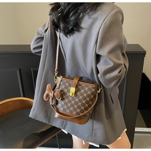 Sac seau marron à monogramme avec garniture en cuir porté par un mannequin en costume gris