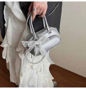 Detail view of silver metallic bag featuring a white lace bow and pearl bead charm