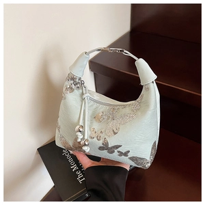 Detail of mint green sequin bag featuring silver butterfly patterns and metal handle