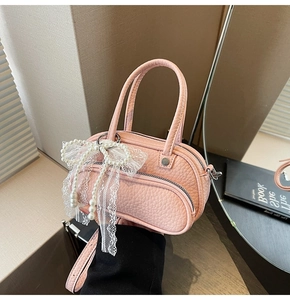 Detail of pink Boston bag with lace bow and pearl charm on a textured leather surface