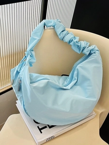 Light blue crescent shoulder bag with ruched strap and nylon texture on a white book