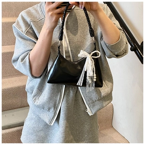 Détail du sac noir brillant avec nœud en dentelle blanche et pendentif perle sur modèle
