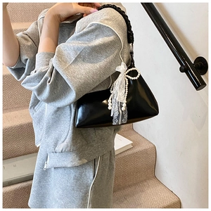 Détail du sac croissant noir brillant avec poignée tressée et ruban en dentelle