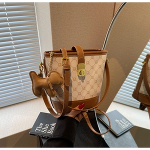 Détail du sac seau bicolore avec fermoir rotatif doré et charm de chien en cuir brun