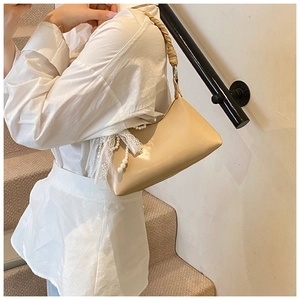 Détail d'un sac hobo beige avec bandoulière tressée, orné de dentelle et perles élégantes