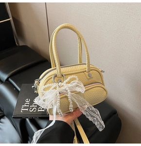 Close-up of yellow pebble grain handbag featuring pearl bow and white lace ribbons