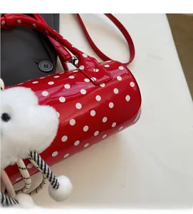 Close-up of a red polka dot cylinder bag with a white plush heart-shaped charm accessory
