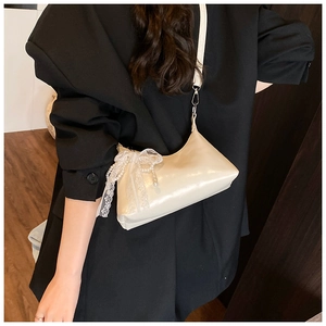 Détail du sac crème avec nœud en dentelle et pendentif perle porté par le mannequin